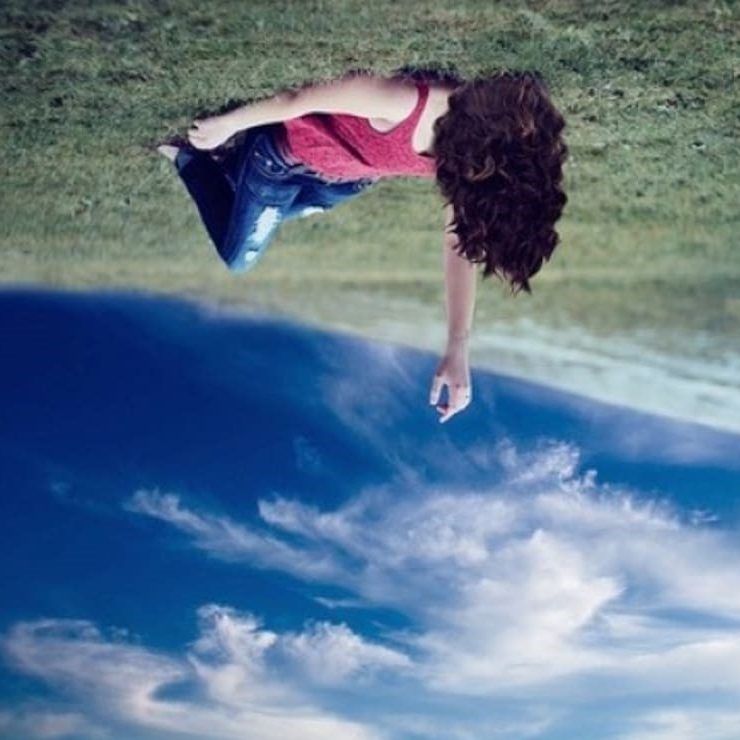 Upside down picture of a person lying down in an open grassy field with sky above them. So the grass is at the top and the sky is at the bottom.