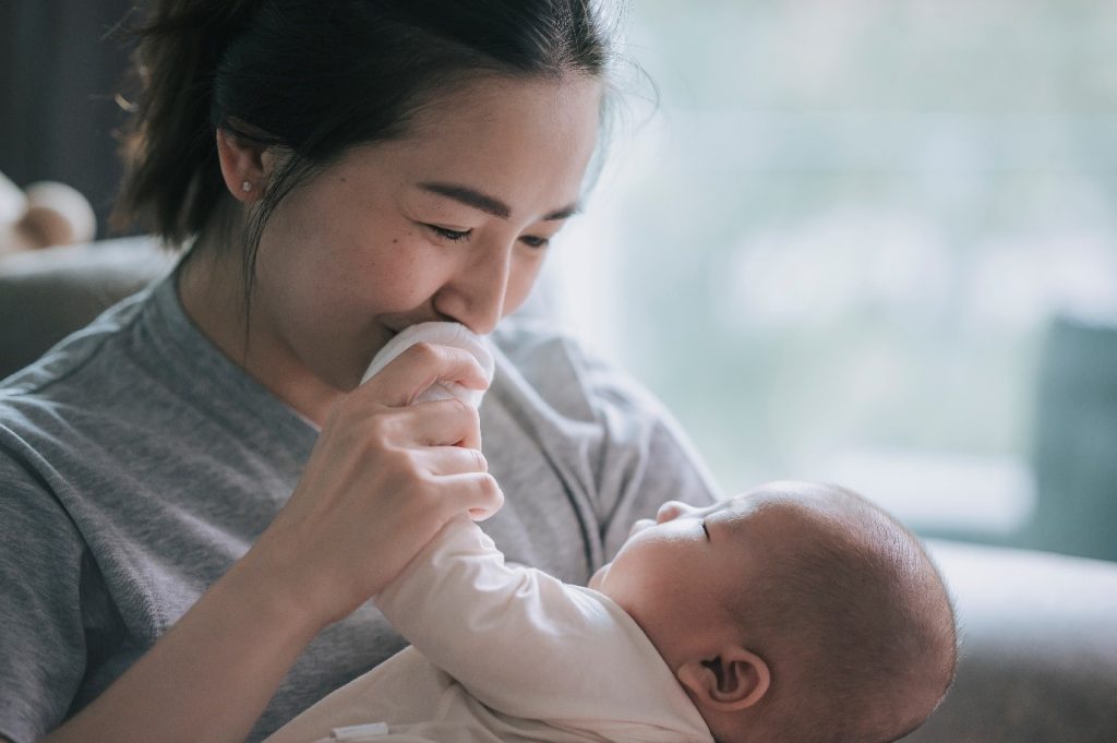 woman holding a baby with the babys hand by her mouth
