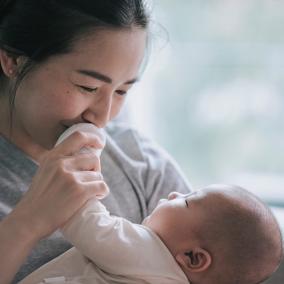 woman holding a baby with the babys hand by her mouth