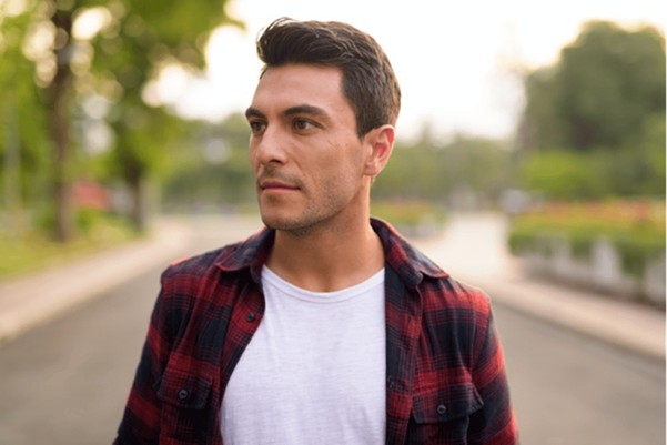 A man wearing a red checkered shirt over a white t shirt standing on a road which is blurred