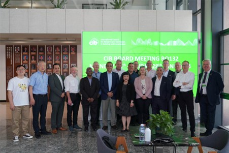 A group of people standing indoors in front of a green banner with text that reads "CIB Board Meeting B0132". The setting appears to be a modern conference space with with a wall displaying framed photographs